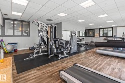Dedicated fitness area featuring wood-finish flooring, a suspended ceiling with integrated lighting, and multiple exercise machines - 