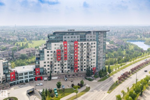 Contemporary multi-story building featuring a facade with red and grey accents, individual balconies, and an adjacent parking area - 5151 Windermere  Bv Sw, Edmonton, AB - Outdoor With View