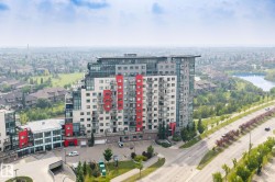 Contemporary multi-story building featuring a facade with red and grey accents, individual balconies, and an adjacent parking area - 