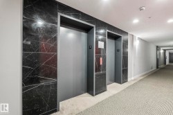 Elevator access within a hallway featuring dark marble-look wall tiling, grey carpeting, and recessed ceiling lighting - 
