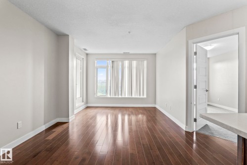 Bright interior space featuring wood-finish flooring, light-toned wall paint, large windows with vertical blinds, and a solid core interior door - 5151 Windermere  Bv Sw, Edmonton, AB - Indoor Photo Showing Other Room