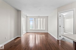 Bright interior space featuring wood-finish flooring, light-toned wall paint, large windows with vertical blinds, and a solid core interior door - 
