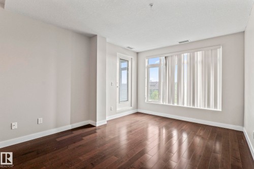 Spacious interior featuring dark wood-finish flooring, light neutral walls, and extensive window light with vertical blinds - 5151 Windermere  Bv Sw, Edmonton, AB - Indoor Photo Showing Other Room