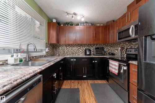 U-shaped kitchen featuring two-tone cabinetry, mosaic tile backsplash, wood-finish flooring, and a stainless steel double basin sink - 17928 93 Ave Nw, Edmonton, AB 