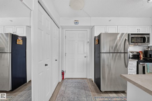 Modern kitchen featuring stainless steel appliances including refrigerator, microwave, and range; light wood-finish countertops; white cabinetry with brushed nickel hardware; and wood-finish flooring throughout - #419 920 156 St Nw, Edmonton, AB 