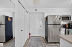 Modern kitchen featuring stainless steel appliances including refrigerator, microwave, and range; light wood-finish countertops; white cabinetry with brushed nickel hardware; and wood-finish flooring throughout - 