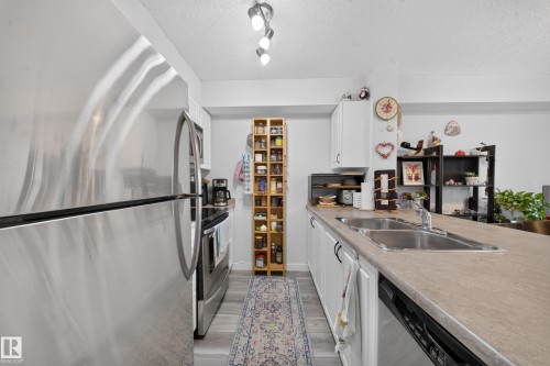 Galley kitchen featuring stainless steel appliances, including a French-door refrigerator and gas cooktop, paired with light-finish countertops and white cabinetry - #419 920 156 St Nw, Edmonton, AB 