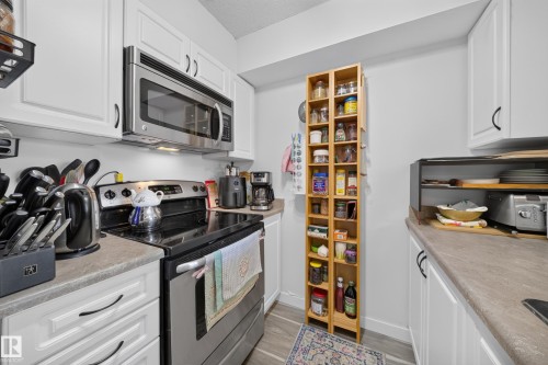 White cabinetry, stainless steel microwave, stainless steel range, light-toned countertops, and wood-finish flooring - #419 920 156 St Nw, Edmonton, AB 