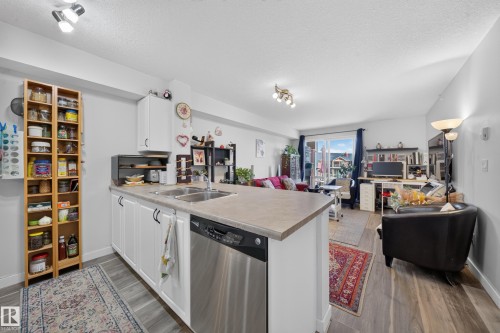 Kitchen island with integrated double basin sink, stainless steel dishwasher, white cabinetry, and a light-toned countertop - #419 920 156 St Nw, Edmonton, AB 