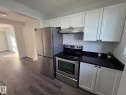 Stainless steel appliances, black countertops, white shaker cabinetry, wood-finish flooring, and recessed lighting - 140 Dickinsfield Court Nw, Edmonton, AB 