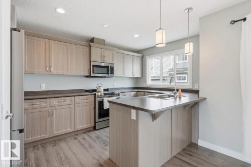 Kitchen featuring wood-finish cabinetry, stainless steel appliances, a double basin sink, recessed lighting, and pendant lights - #12 1391 Starling Dr Nw, Edmonton, AB 