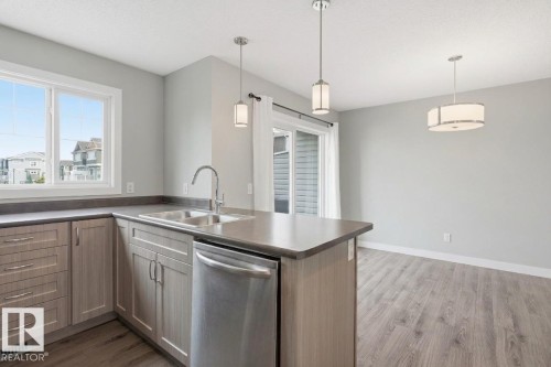 Kitchen featuring a double basin stainless steel sink, a stainless steel dishwasher, modern pendant lighting, and wood-finish flooring - #12 1391 Starling Dr Nw, Edmonton, AB 