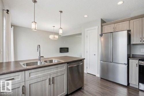 Kitchen featuring a double basin stainless steel sink, stainless steel appliances, wood-finish flooring, recessed lighting, and pendant lighting - #12 1391 Starling Dr Nw, Edmonton, AB 