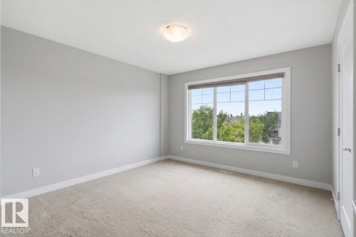 Neutral wall color, wall-to-wall carpeting, contemporary ceiling light fixture, large window with white framing - #12 1391 Starling Dr Nw, Edmonton, AB 