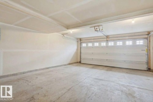 Attached garage featuring a concrete floor, painted walls, and a paneled garage door with upper window inserts - #12 1391 Starling Dr Nw, Edmonton, AB 