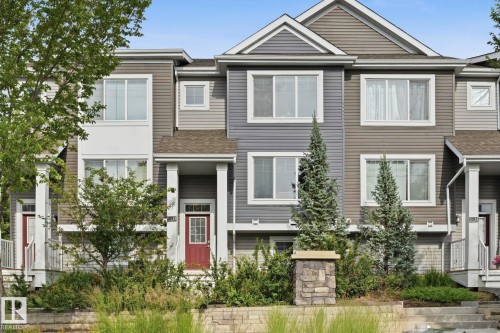 Multi-level townhouse exterior featuring multiple window styles, columns at the entry, and an integrated landscaping bed with plantings - #12 1391 Starling Dr Nw, Edmonton, AB 