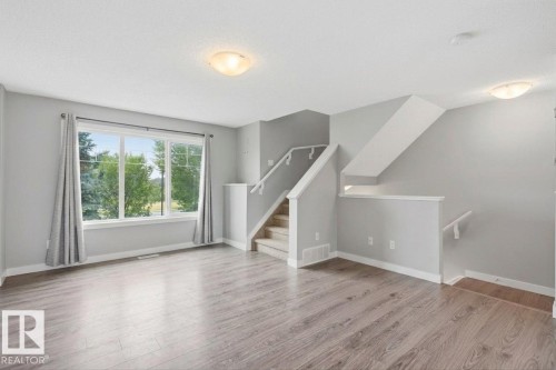 Spacious interior featuring wood-finish flooring, a multi-pane window, and a carpeted staircase with white railings - #12 1391 Starling Dr Nw, Edmonton, AB 