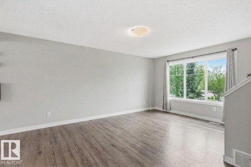 Spacious room with wood-finish flooring, a large multi-pane window, and a flush-mount ceiling light fixture - #12 1391 Starling Dr Nw, Edmonton, AB 