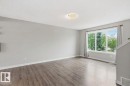 Spacious room with wood-finish flooring, a large multi-pane window, and a flush-mount ceiling light fixture - #12 1391 Starling Dr Nw, Edmonton, AB 
