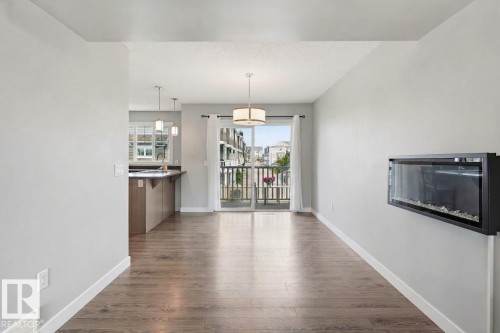 Wood-finish flooring throughout, with a wall-mounted electric fireplace, and a sliding glass door providing access to a balcony with metal railings - #12 1391 Starling Dr Nw, Edmonton, AB 