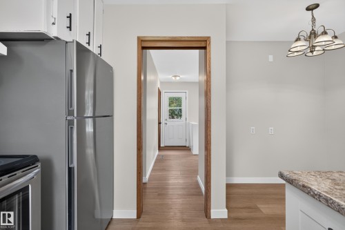Stainless steel refrigerator, white cabinetry with black hardware, wood-finish flooring, and a multi-light chandelier - 2 Grandora Crescent, St. Albert, AB 
