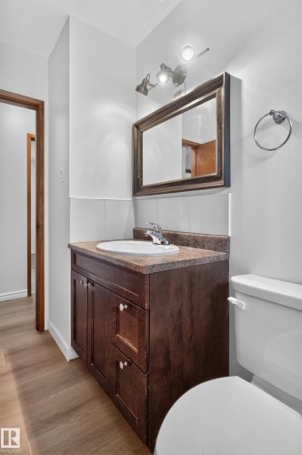 Wood-finish flooring, dark wood vanity with a white basin, stone-look countertop, and a decorative framed mirror - 2 Grandora Crescent, St. Albert, AB 
