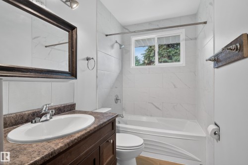 Bathroom featuring a white bathtub, tiled shower surround, framed mirror, vanity with an integrated sink, and a window - 2 Grandora Crescent, St. Albert, AB 