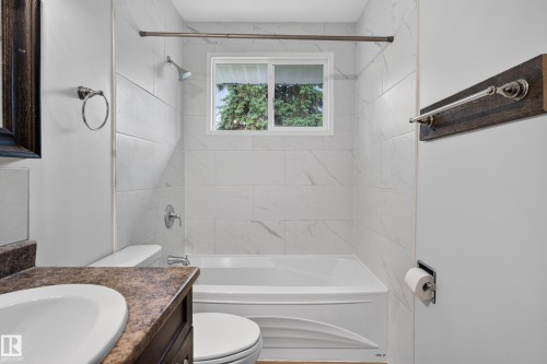 Bathtub with shower fixture, white subway tile surround, window with exterior scenery, and vanity with integrated sink - 2 Grandora Crescent, St. Albert, AB 