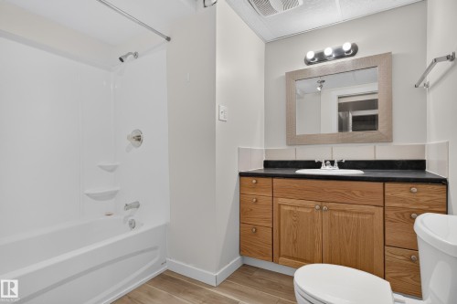 Spa-inspired primary bathroom featuring a wood-finish vanity with dual sinks, black countertop, framed mirror with integrated lighting, and chrome fixtures - 2 Grandora Crescent, St. Albert, AB 