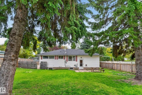 Expansive backyard with a manicured lawn, established perimeter fencing, mature trees, and a ground-level patio - 2 Grandora Crescent, St. Albert, AB 