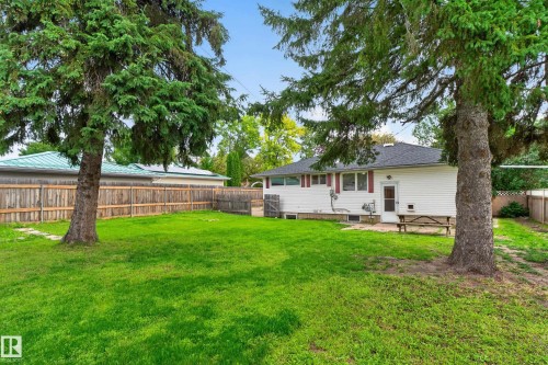 Expansive green lawn framed by mature trees, privacy fencing, and a white siding exterior - 2 Grandora Crescent, St. Albert, AB 