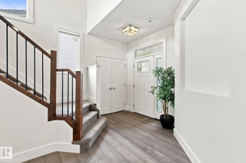 Two-story entryway featuring wood-finish flooring, a white paneled entry door with transom and sidelights, and a wood and iron baluster staircase - 4530 Saly Place Sw, Edmonton, AB 