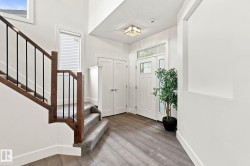Two-story entryway featuring wood-finish flooring, a white paneled entry door with transom and sidelights, and a wood and iron baluster staircase - 