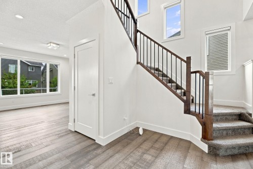 Wood-finish flooring, staircase with dark wood newel posts and metal spindles, carpeted stairs, recessed lighting, and large windows with white trim - 4530 Saly Place Sw, Edmonton, AB 
