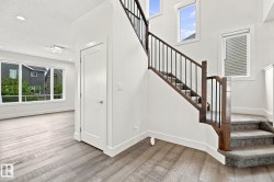 Wood-finish flooring, staircase with dark wood newel posts and metal spindles, carpeted stairs, recessed lighting, and large windows with white trim - 