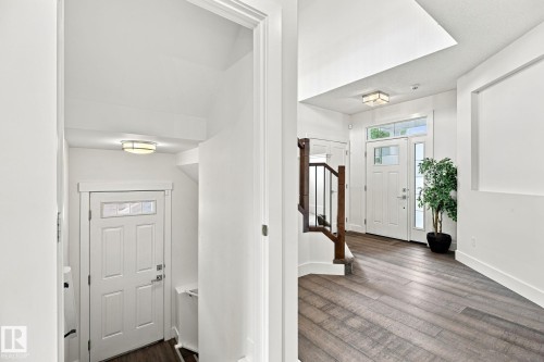 Two-story entryway with wood-finish flooring, white paneled doors, staircase with dark wood handrail and black metal spindles, and recessed lighting - 4530 Saly Place Sw, Edmonton, AB 