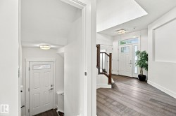 Two-story entryway with wood-finish flooring, white paneled doors, staircase with dark wood handrail and black metal spindles, and recessed lighting - 