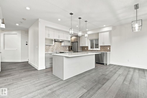 Kitchen featuring a center island, white cabinetry, integrated stainless steel appliances, mosaic tile backsplash, and wood-finish flooring - 4530 Saly Place Sw, Edmonton, AB 