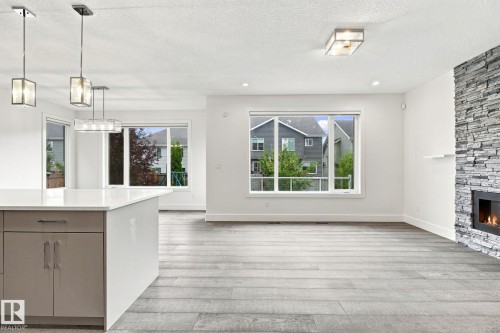 Spacious interior featuring wood-finish flooring, a contemporary fireplace with a stone surround, and an integrated kitchen island with a light-toned countertop - 4530 Saly Place Sw, Edmonton, AB 