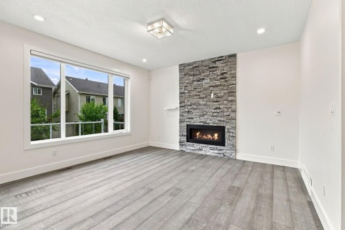Expansive window, wood-finish flooring, recessed lighting, gas fireplace with a stone surround, and a ceiling-mounted light fixture - 4530 Saly Place Sw, Edmonton, AB 