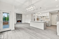 Open-concept living area featuring wood-finish flooring, a stone-clad fireplace, and a kitchen with white cabinetry and a center island - 