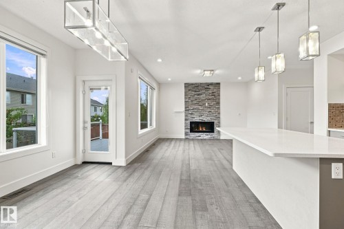 Wide plank wood-finish flooring, stone-clad fireplace, built-in kitchen island with countertop, recessed lighting, and modern pendant fixtures - 4530 Saly Place Sw, Edmonton, AB 