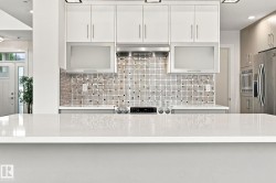 White quartz countertop, mosaic tile backsplash, stainless steel range hood, stainless steel refrigerator, and built-in stainless steel microwave - 