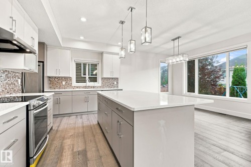 Contemporary kitchen with light wood-finish flooring, white cabinetry, a large kitchen island with a light countertop, and stainless steel appliances - 4530 Saly Place Sw, Edmonton, AB 