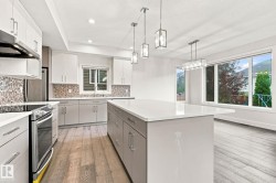 Contemporary kitchen with light wood-finish flooring, white cabinetry, a large kitchen island with a light countertop, and stainless steel appliances - 