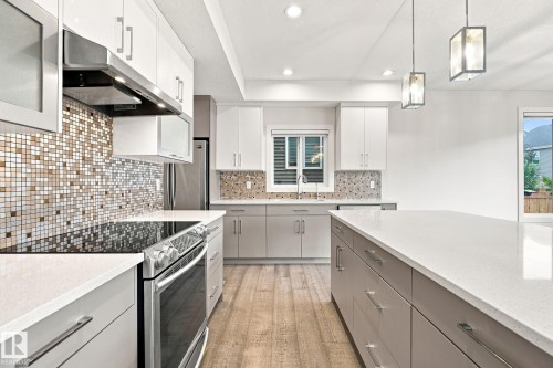 Modern kitchen featuring a mosaic tile backsplash, stainless steel appliances, light wood-finish flooring, white countertops, and recessed lighting - 4530 Saly Place Sw, Edmonton, AB 