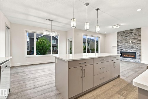 Kitchen island with a light-toned countertop, wood-finish flooring, recessed lighting, and pendant lighting fixtures - 4530 Saly Place Sw, Edmonton, AB 