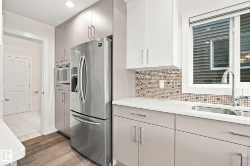 Kitchen featuring stainless steel appliances, mosaic tile backsplash, wood-finish flooring, and white countertops - 4530 Saly Place Sw, Edmonton, AB 