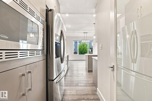 Stainless steel microwave and refrigerator, light-toned cabinetry, and wood-finish flooring - 4530 Saly Place Sw, Edmonton, AB 