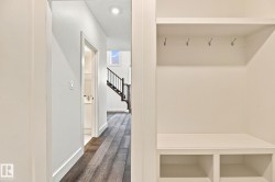 Built-in entryway storage with shelving and hooks, featuring wood-finish flooring and a visible staircase with dark railings - 